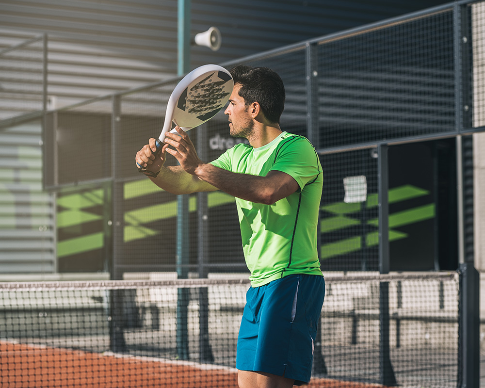 Joueur tenant sa raquette à deux mains sur un terrain de padel extérieur au sein d’un complexe sportif dédié aux sports de raquette.